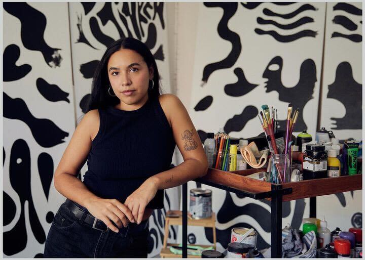 Image of Zoe next to her painting cart, surrounded by black and white abstract paintings.